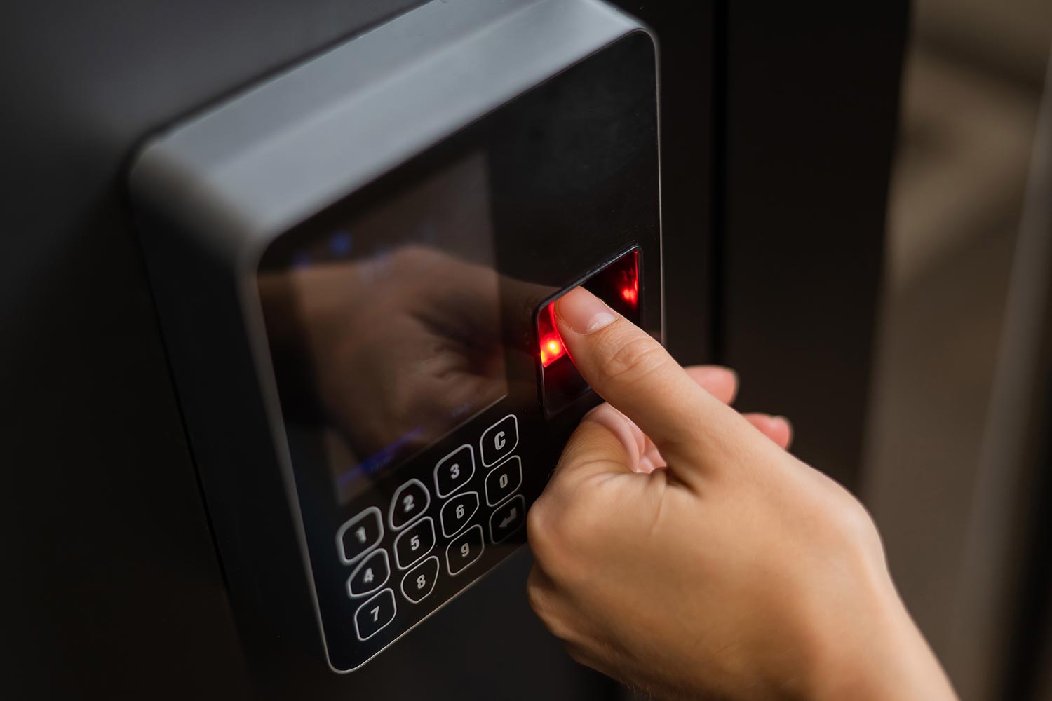 Close-up of a finger pressing a biometric fingerprint scanner on a security keypad