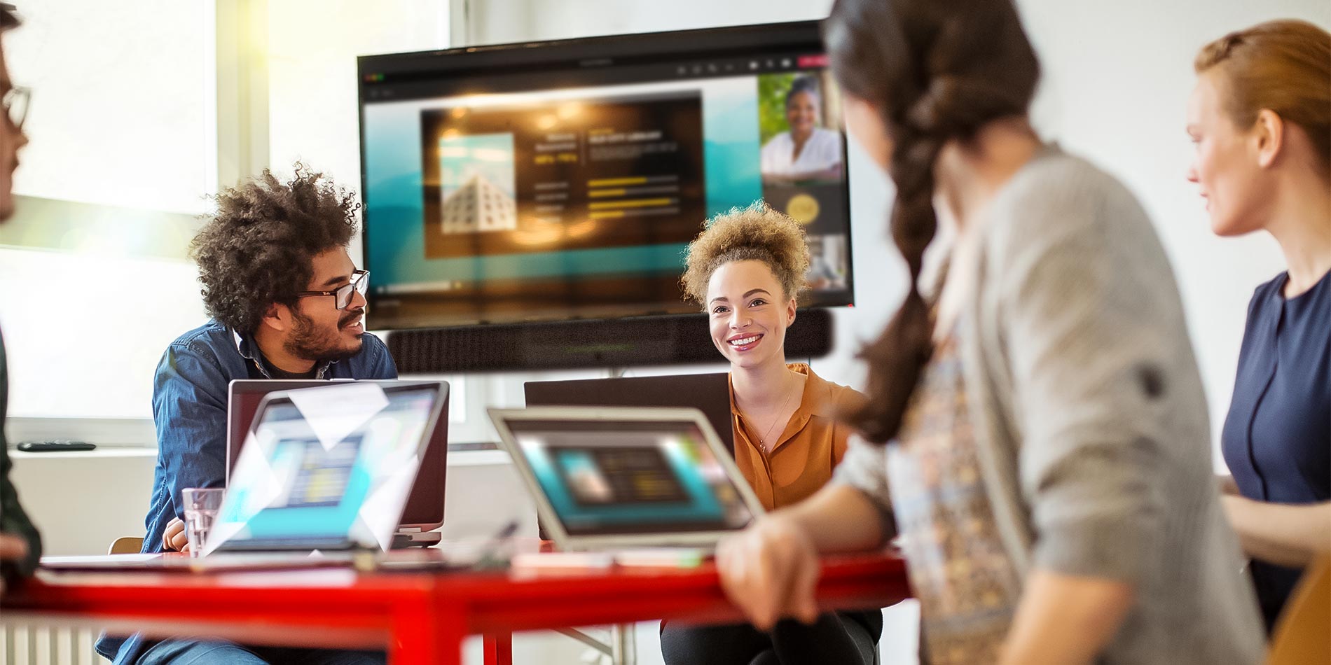 People discussing in a brightly lit office meeting room with a video conferencing screen