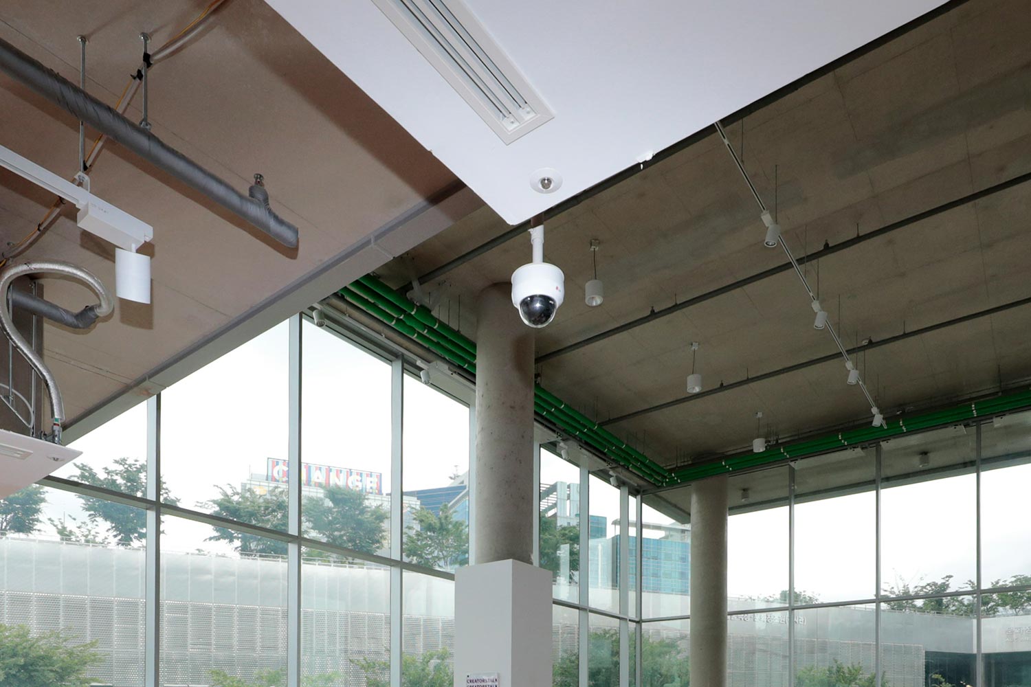 White dome security camera mounted on an industrial ceiling with large windows